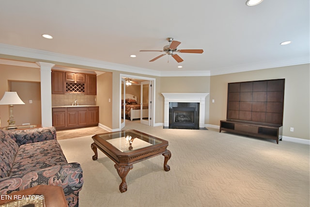 carpeted living room featuring ceiling fan, ornamental molding, sink, and decorative columns