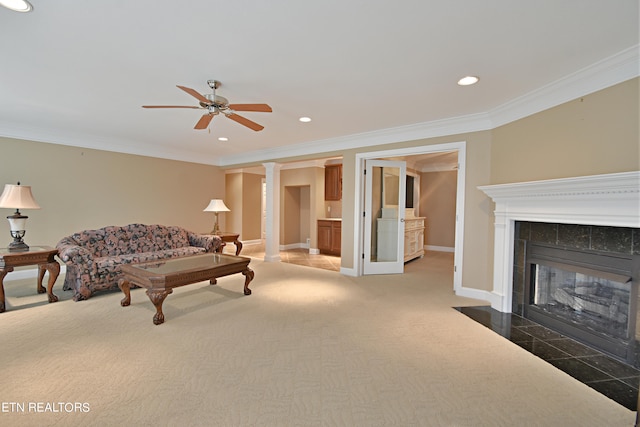 carpeted bedroom with a tile fireplace, ensuite bathroom, decorative columns, ornamental molding, and ceiling fan