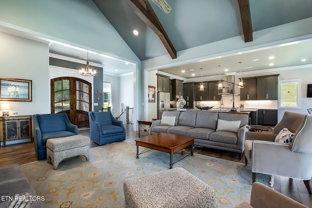 living room featuring an inviting chandelier, crown molding, lofted ceiling with beams, french doors, and light hardwood / wood-style floors