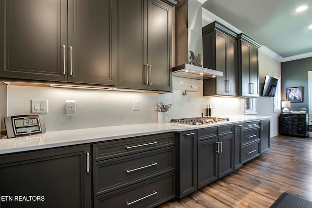 kitchen featuring crown molding, tasteful backsplash, wood-type flooring, stainless steel gas stovetop, and wall chimney exhaust hood