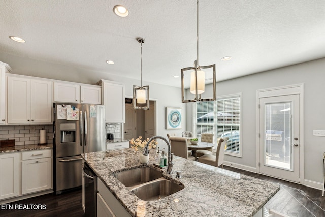 kitchen with sink, stainless steel appliances, backsplash, a kitchen island with sink, and white cabinets