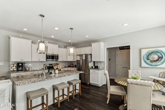 kitchen with sink, dark wood-type flooring, pendant lighting, a center island with sink, and appliances with stainless steel finishes