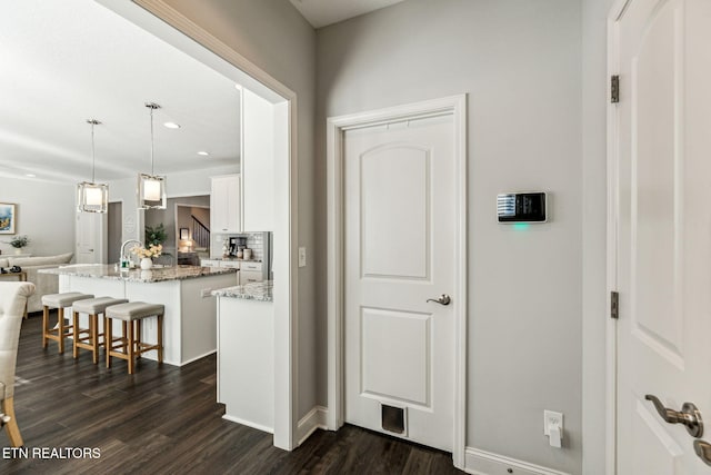 kitchen with pendant lighting, a kitchen island with sink, a kitchen breakfast bar, dark hardwood / wood-style flooring, and white cabinetry