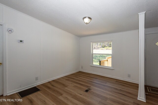 empty room featuring visible vents, a textured ceiling, and wood finished floors