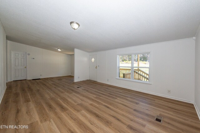 unfurnished living room featuring visible vents, a textured ceiling, baseboards, and wood finished floors