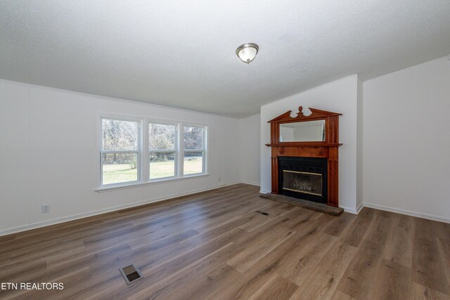 unfurnished living room featuring visible vents, wood finished floors, a textured ceiling, and a glass covered fireplace