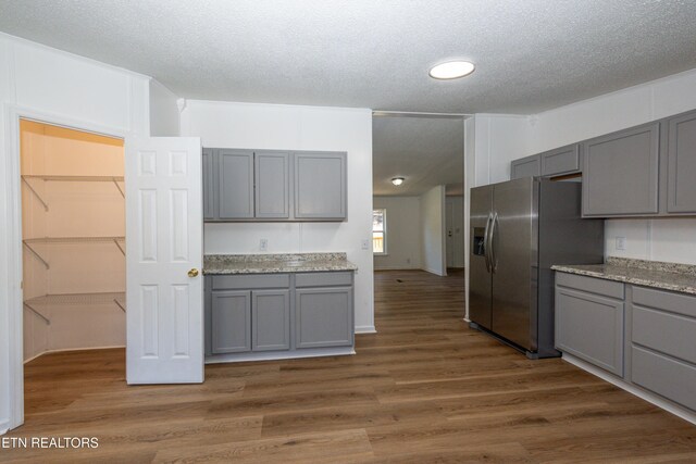 kitchen with a textured ceiling, gray cabinetry, dark wood-style flooring, and stainless steel fridge with ice dispenser