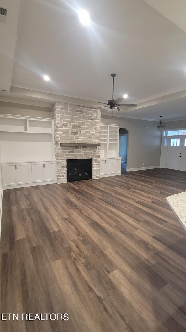 unfurnished living room featuring a stone fireplace, ceiling fan, and dark wood-type flooring