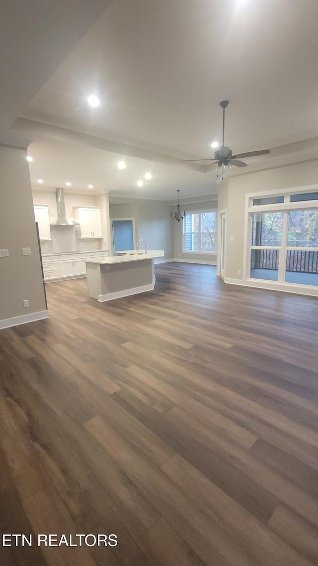 unfurnished living room with sink, ceiling fan with notable chandelier, and dark hardwood / wood-style floors