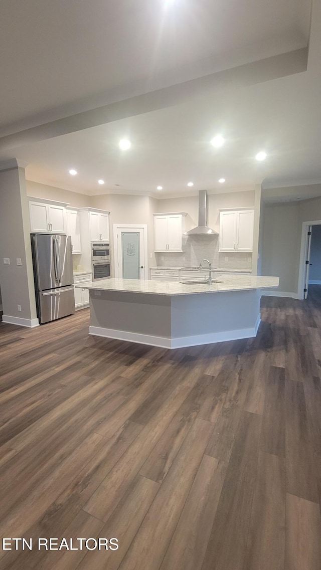 kitchen featuring white cabinetry, a large island, wall chimney exhaust hood, dark wood-type flooring, and appliances with stainless steel finishes