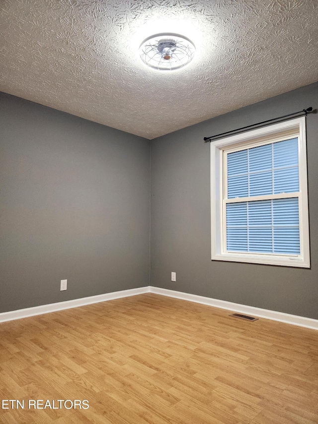 spare room with a textured ceiling and light wood-type flooring