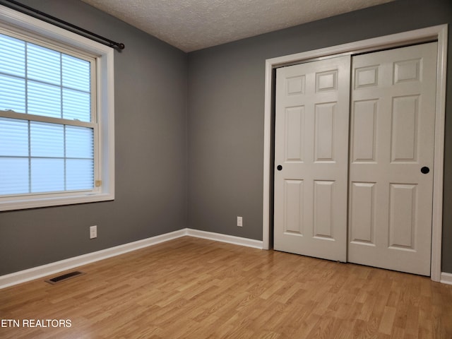 unfurnished bedroom featuring a textured ceiling, light hardwood / wood-style flooring, and a closet