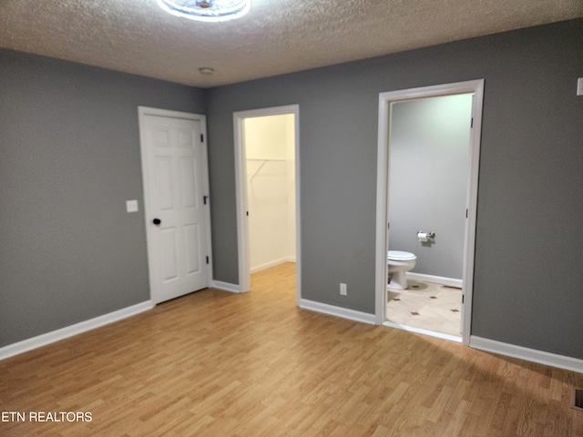 unfurnished bedroom with light hardwood / wood-style flooring, a spacious closet, a textured ceiling, connected bathroom, and a closet