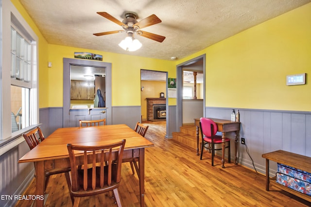 dining room featuring light wood-type flooring, ceiling fan, a fireplace, and a textured ceiling