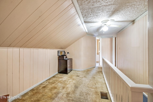 bonus room with lofted ceiling, carpet, wood walls, ceiling fan, and a textured ceiling