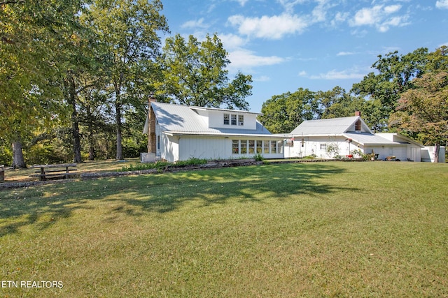 rear view of property with metal roof, a lawn, and a chimney