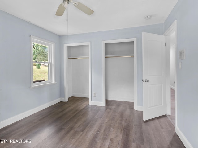 unfurnished bedroom with two closets, ceiling fan, and dark hardwood / wood-style floors