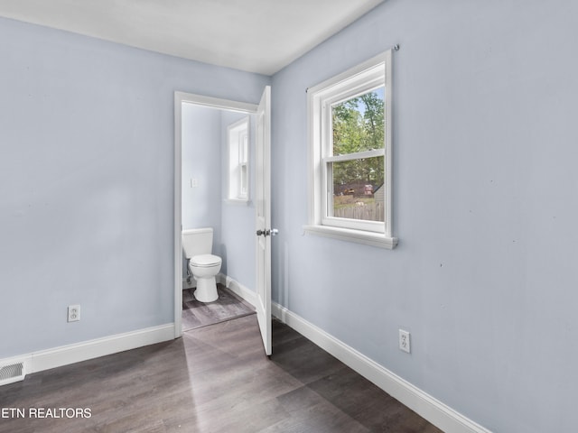 unfurnished bedroom featuring ensuite bathroom and dark wood-type flooring