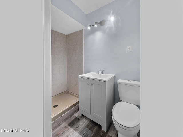 bathroom with tiled shower, vanity, wood-type flooring, and toilet