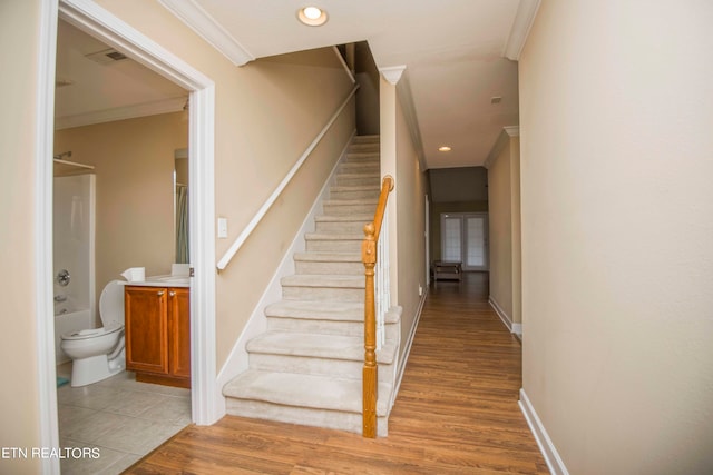 stairway with crown molding and wood-type flooring