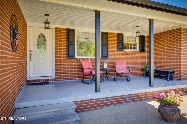 view of exterior entry with a porch and brick siding