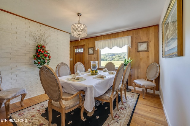 dining area with light wood-type flooring, ornamental molding, wood walls, and brick wall