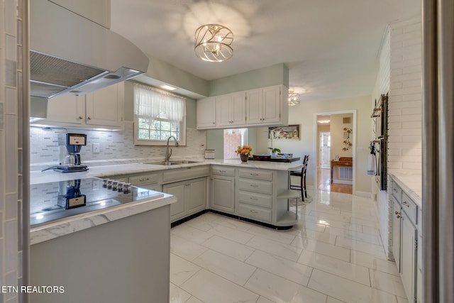 kitchen with decorative backsplash, white cabinets, kitchen peninsula, range hood, and sink