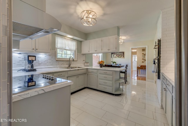 kitchen featuring a peninsula, ventilation hood, backsplash, and a sink