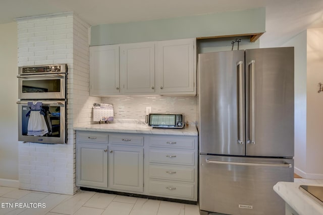 kitchen featuring light stone counters, a toaster, backsplash, appliances with stainless steel finishes, and baseboards