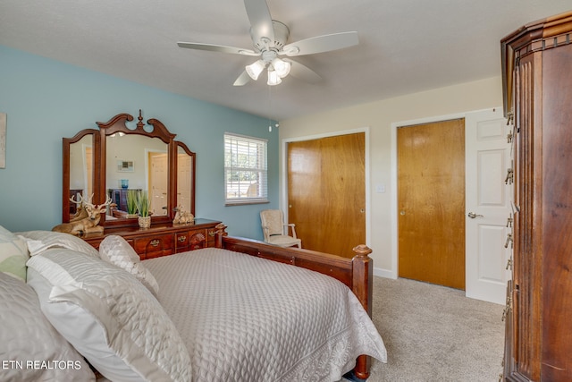 bedroom with ceiling fan, light colored carpet, and two closets