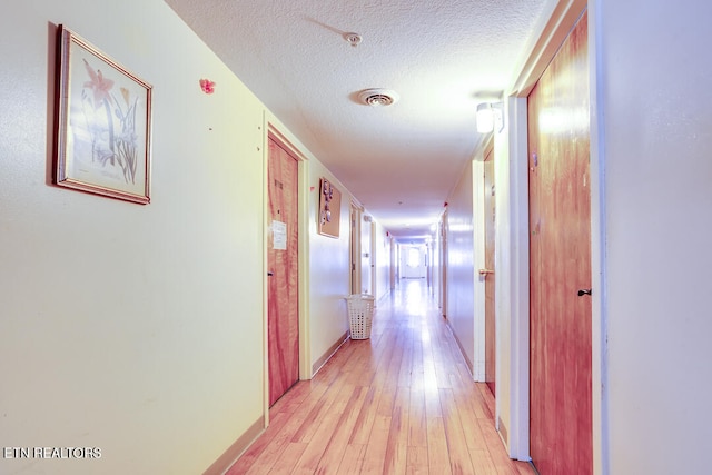 corridor with a textured ceiling and light hardwood / wood-style flooring