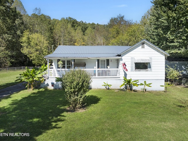 view of front facade featuring metal roof, covered porch, fence, a front yard, and a view of trees