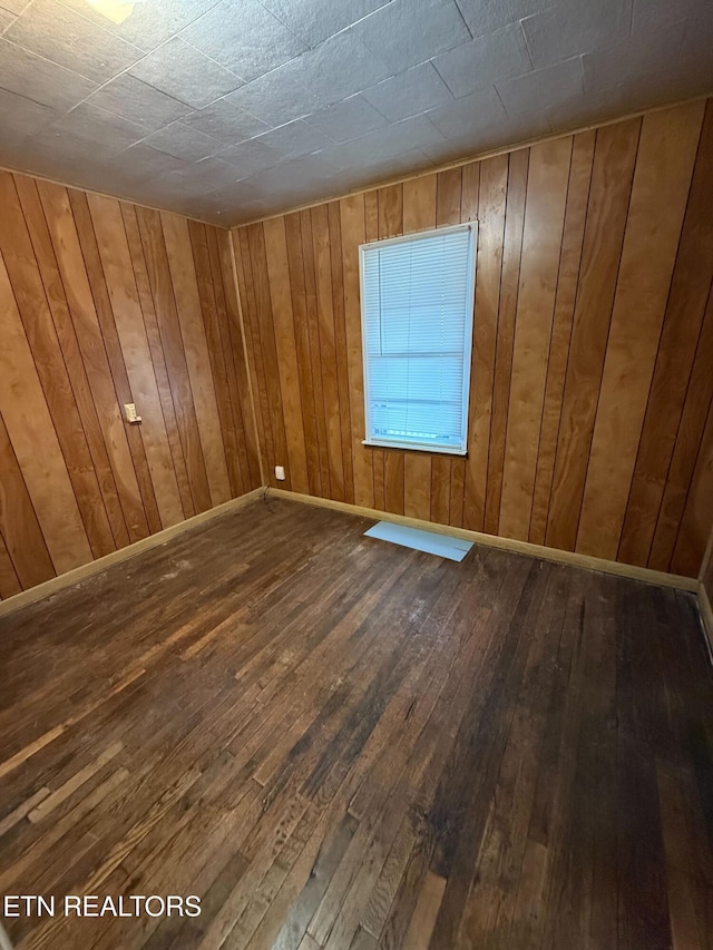 empty room with baseboards, hardwood / wood-style flooring, and wooden walls