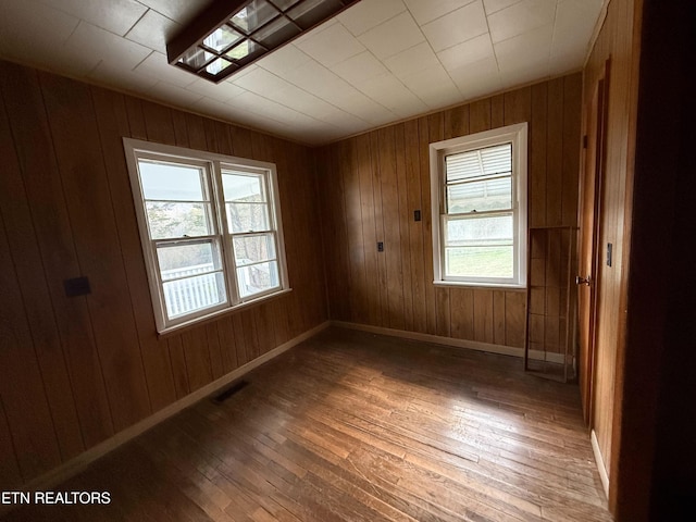 unfurnished room featuring wooden walls, hardwood / wood-style floors, visible vents, and baseboards