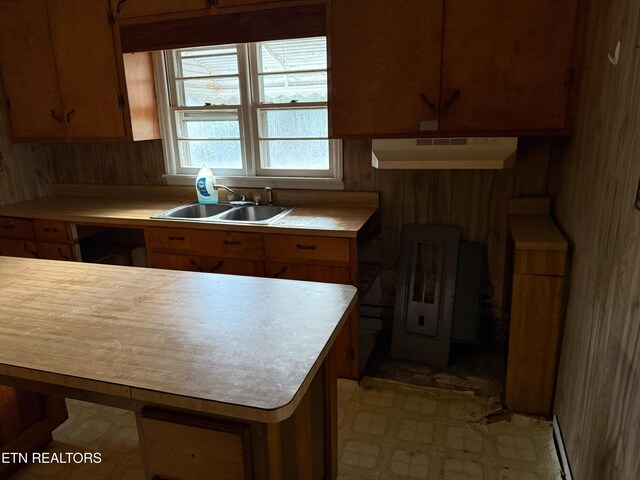 kitchen with wooden walls, under cabinet range hood, a sink, light countertops, and brown cabinetry