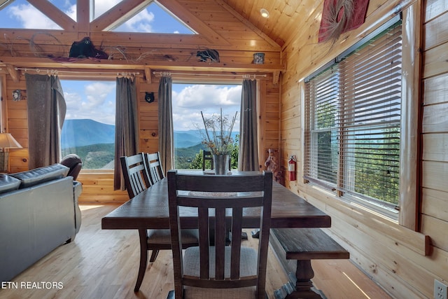 dining area with a mountain view, plenty of natural light, lofted ceiling, and wood walls