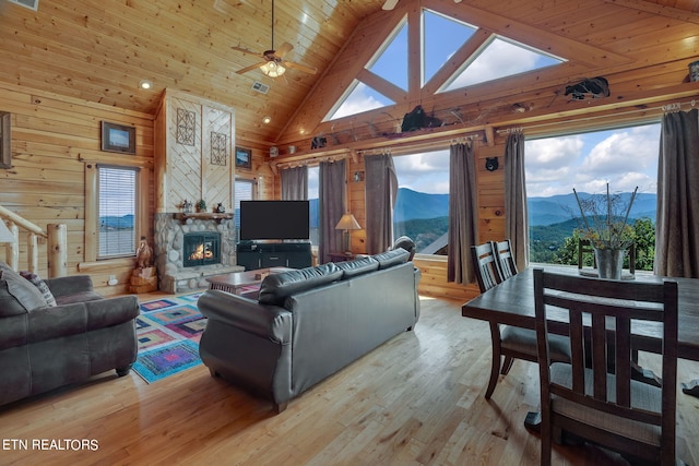 living room featuring wood walls, high vaulted ceiling, ceiling fan, light wood-type flooring, and a fireplace