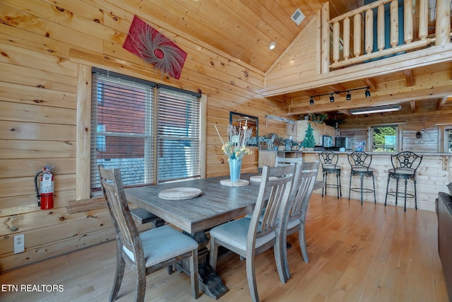 dining area featuring wood walls, high vaulted ceiling, rail lighting, light hardwood / wood-style floors, and wood ceiling