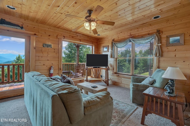 carpeted living room with ceiling fan, wood ceiling, and wooden walls