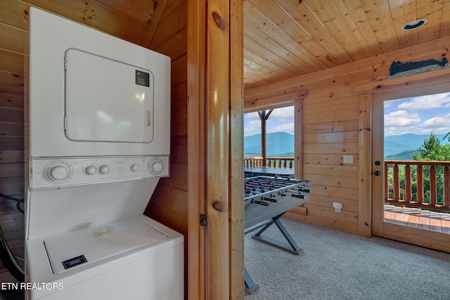 laundry room with carpet, a mountain view, wood walls, wooden ceiling, and stacked washer / dryer