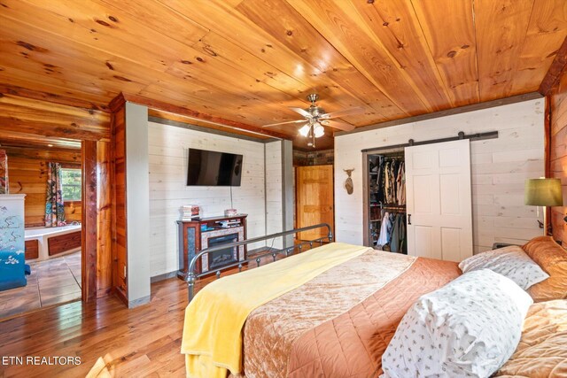 bedroom with wooden ceiling, hardwood / wood-style flooring, a barn door, and wooden walls