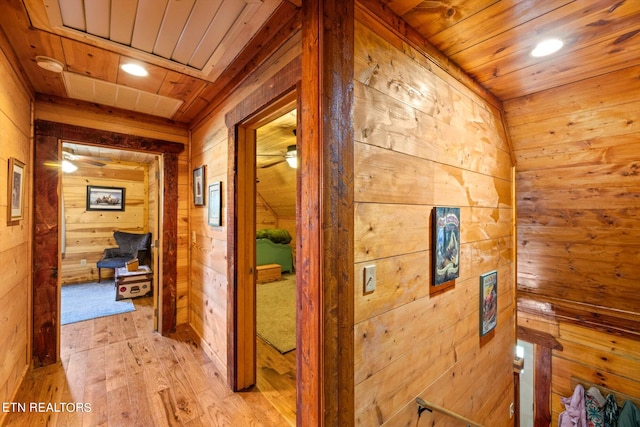 hall with light wood-type flooring, wooden walls, and wooden ceiling