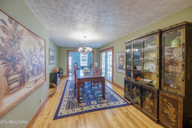 dining area featuring a textured ceiling, a notable chandelier, and light hardwood / wood-style floors