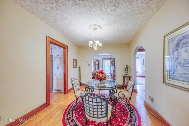 dining area featuring light wood-type flooring, an inviting chandelier, and a textured ceiling