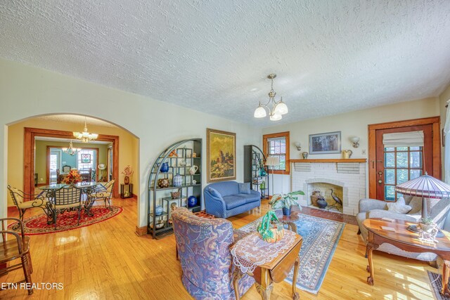 living room featuring light hardwood / wood-style floors, a chandelier, a textured ceiling, and a brick fireplace