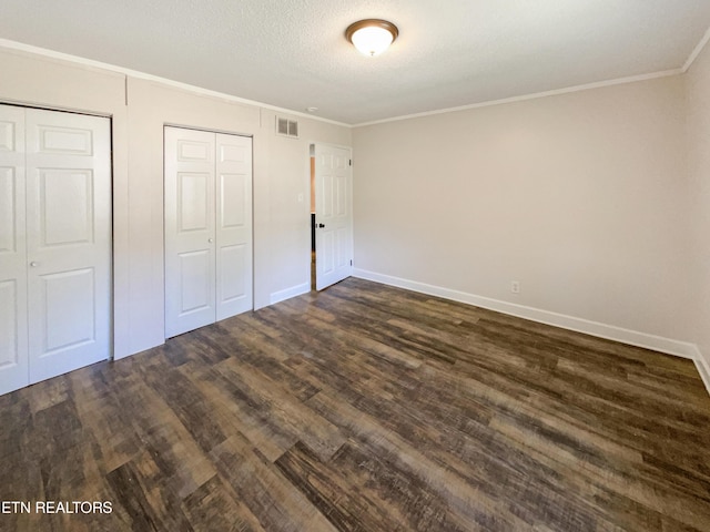 unfurnished bedroom with visible vents, dark wood-type flooring, ornamental molding, a textured ceiling, and baseboards