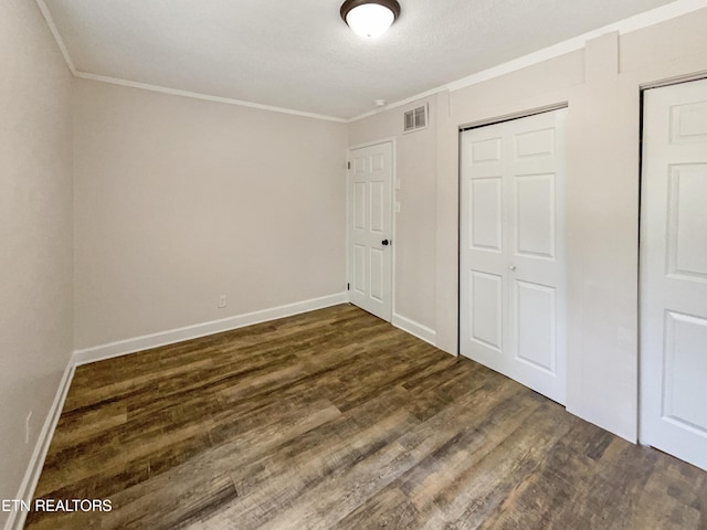 unfurnished bedroom featuring visible vents, baseboards, a closet, ornamental molding, and dark wood-style floors