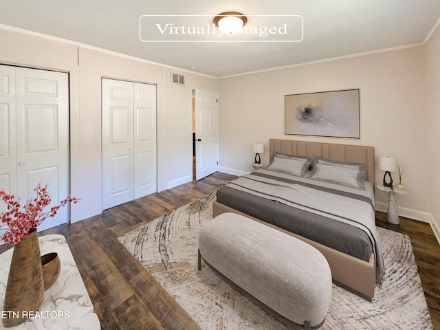 bedroom with visible vents, two closets, crown molding, baseboards, and wood finished floors