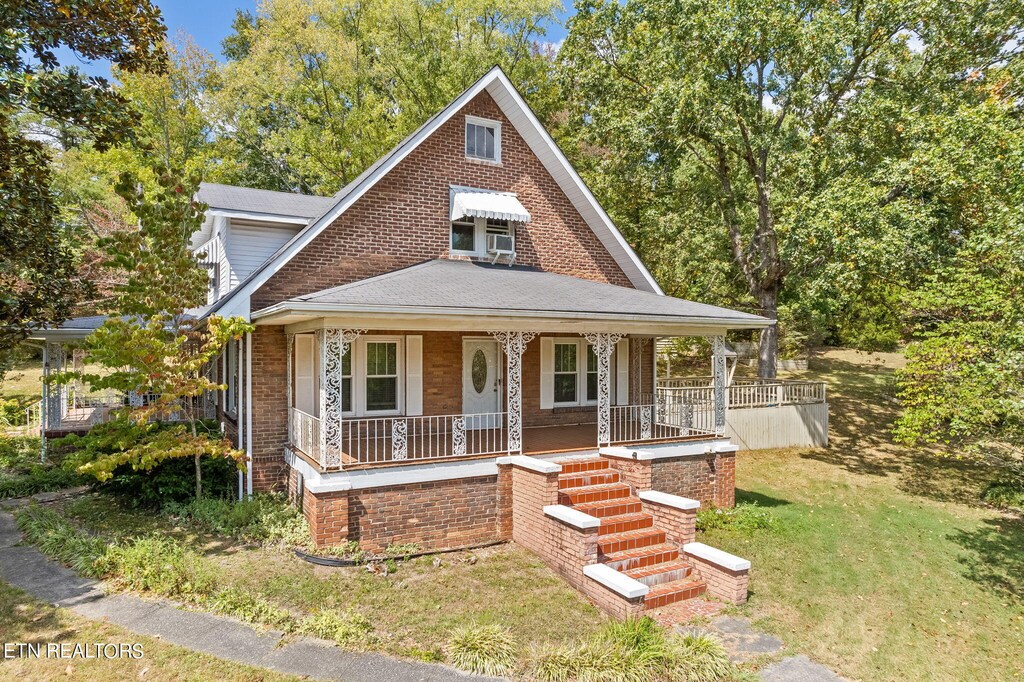 view of front of house with a front yard, brick siding, and covered porch