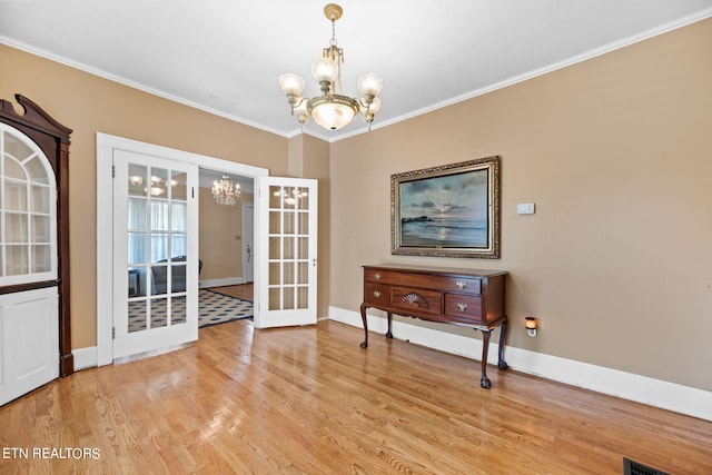 unfurnished dining area featuring french doors, ornamental molding, a chandelier, and light hardwood / wood-style floors